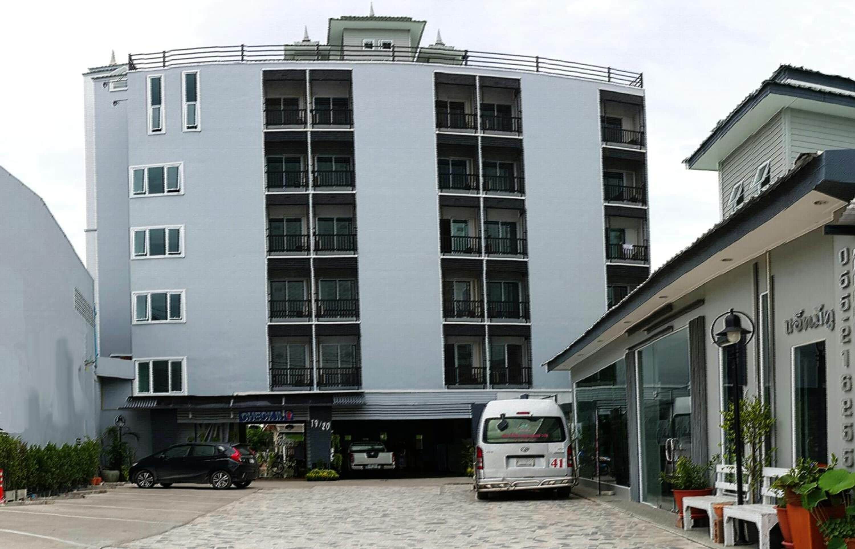 Ein mehrstöckiges Gebäude mit einer geschwungenen Fassade, einem Eingang im Erdgeschoss und einem sichtbaren Parkplatz.