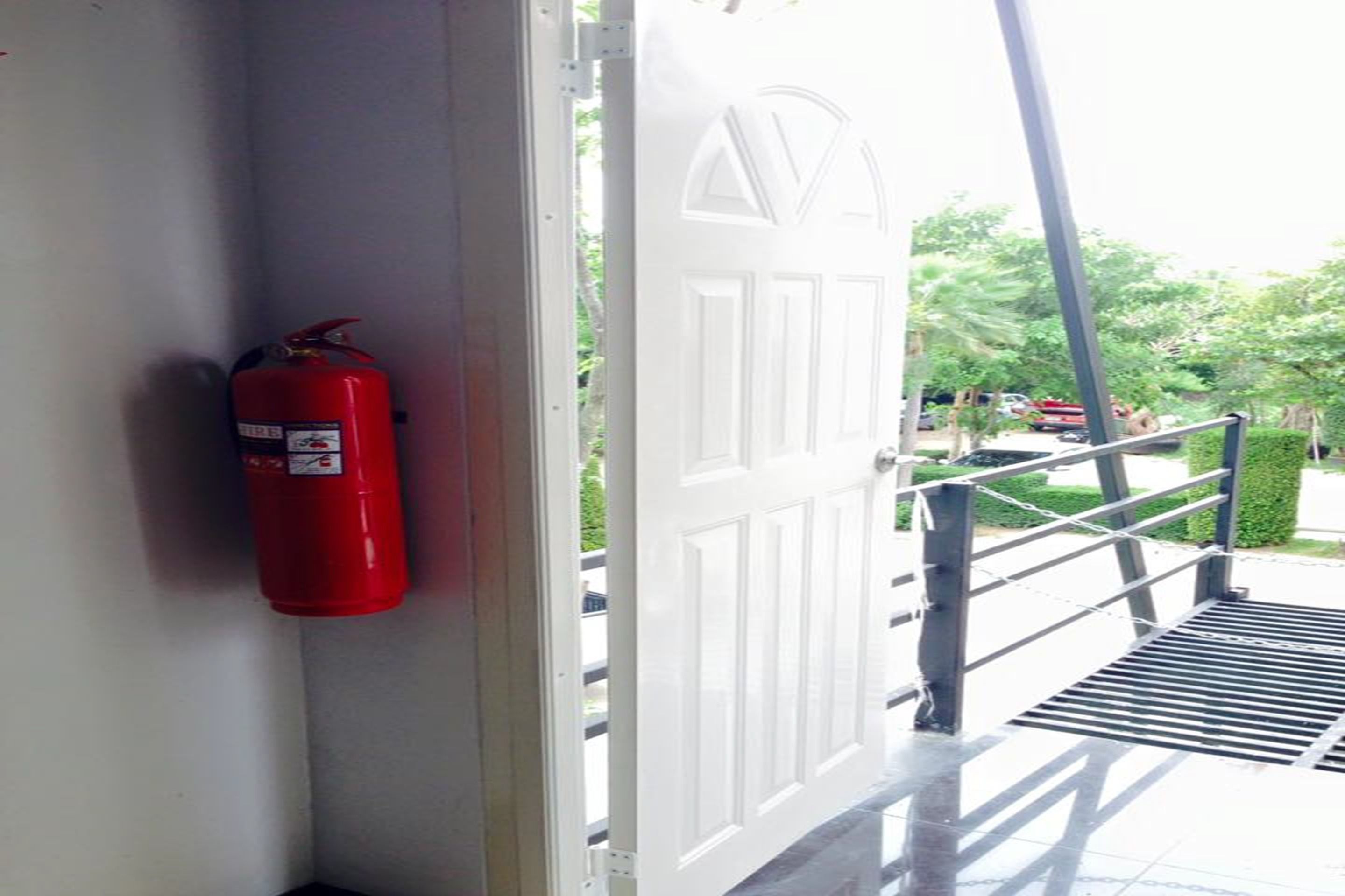 A white door with a metal handrail and a red fire extinguisher mounted on the wall beside it.