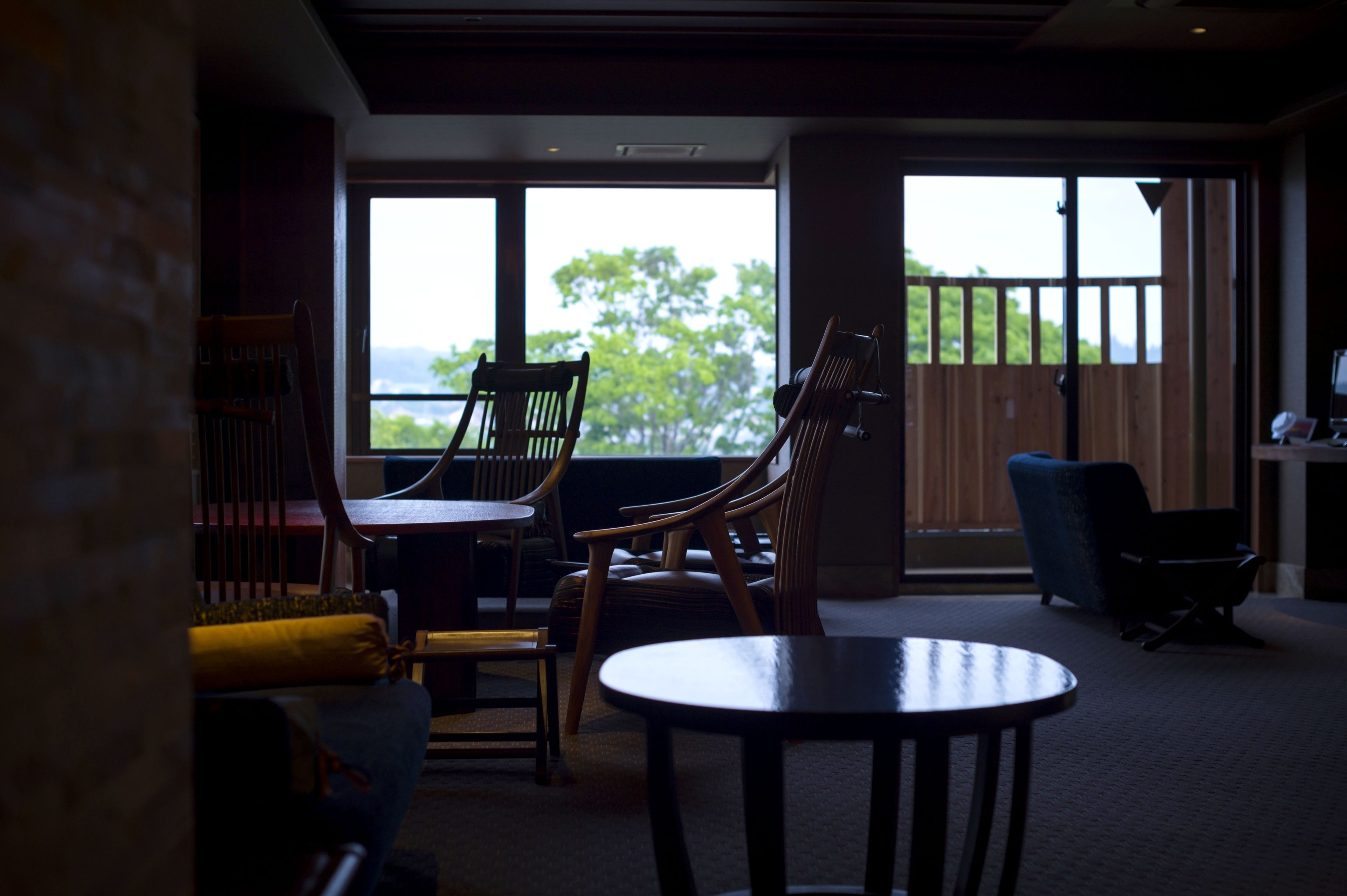 A room with a large window, wooden furniture, and a view of greenery outside.