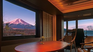A room with a large window overlooking a mountain, a round table with chairs, and a vase with flowers.