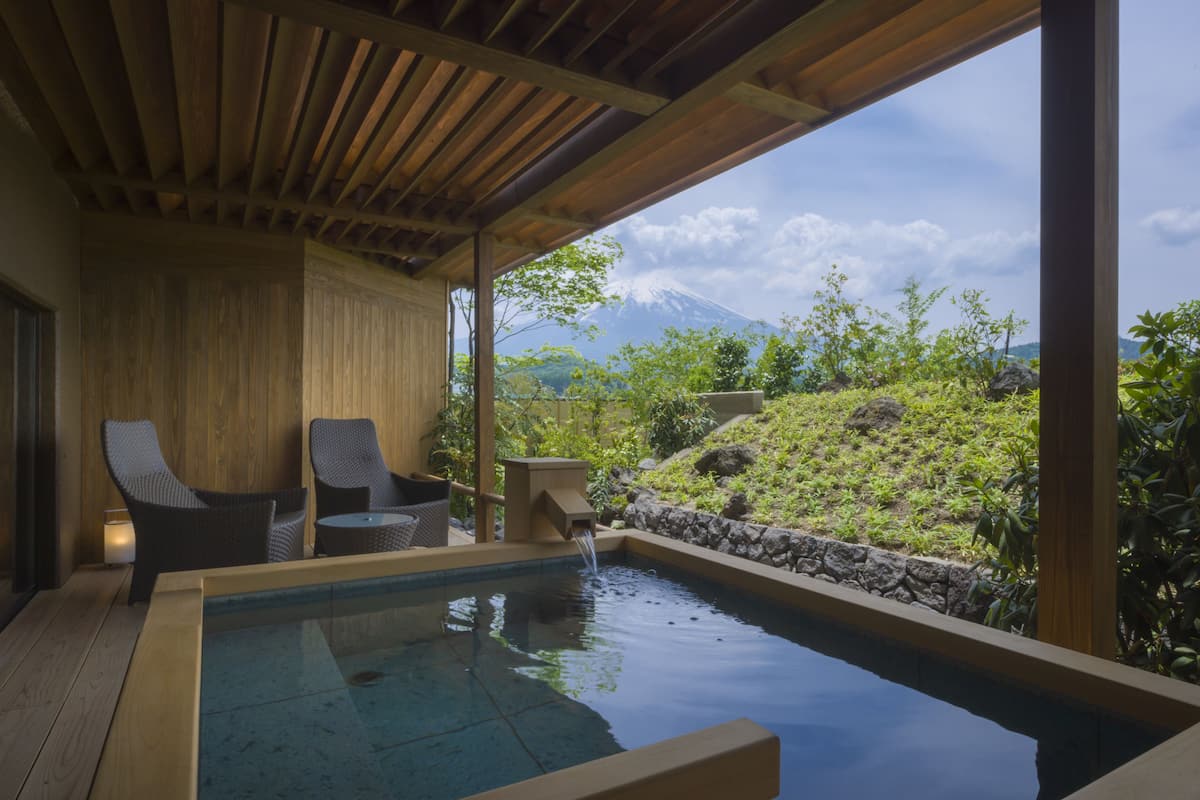 Eine Holzterrasse mit Whirlpool, zwei Korbstühlen und einer Steinmauer.