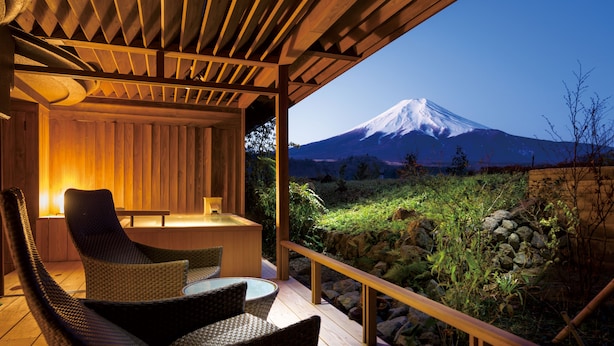 A wooden deck with wicker chairs and a table, overlooking a snow-capped mountain.