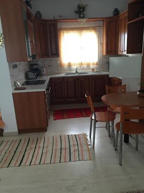 A compact kitchen with wooden cabinets, a sink, a stove, and a dining area with a table and chairs. - Kavousanos Apartments (Agios Nikolaos)