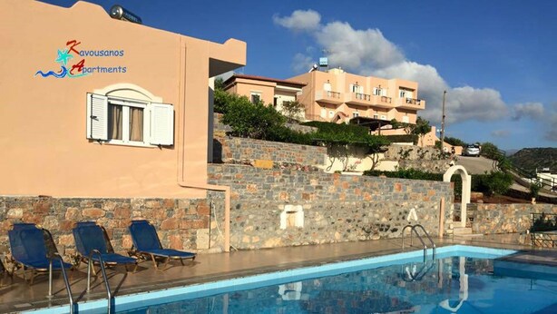 A swimming pool with lounge chairs, a stone wall, and a building with balconies.