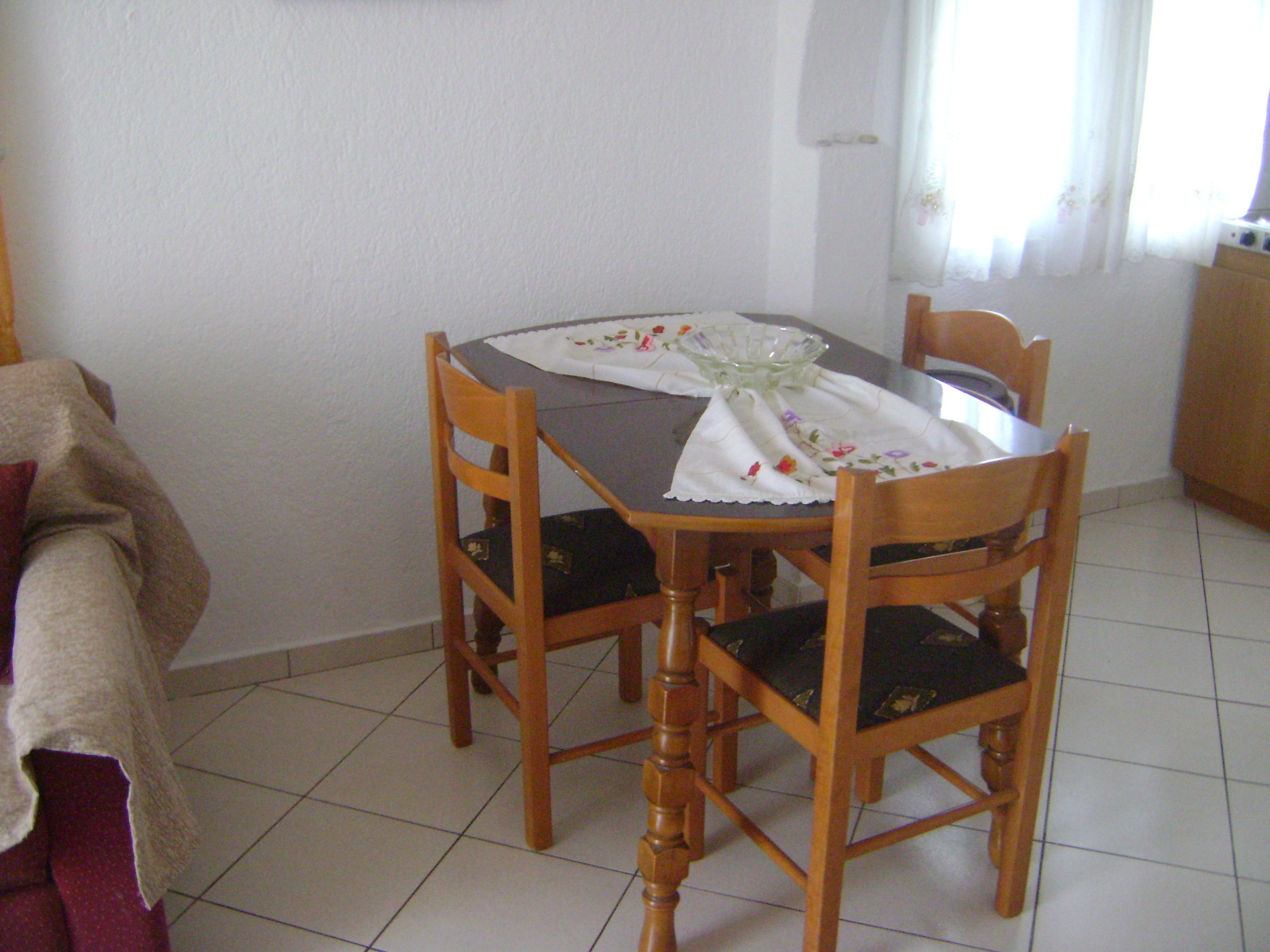 A dining table with a white tablecloth and a glass bowl, surrounded by wooden chairs with black cushions.