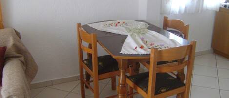 A dining table with a white tablecloth and a glass bowl, surrounded by wooden chairs with black cushions.