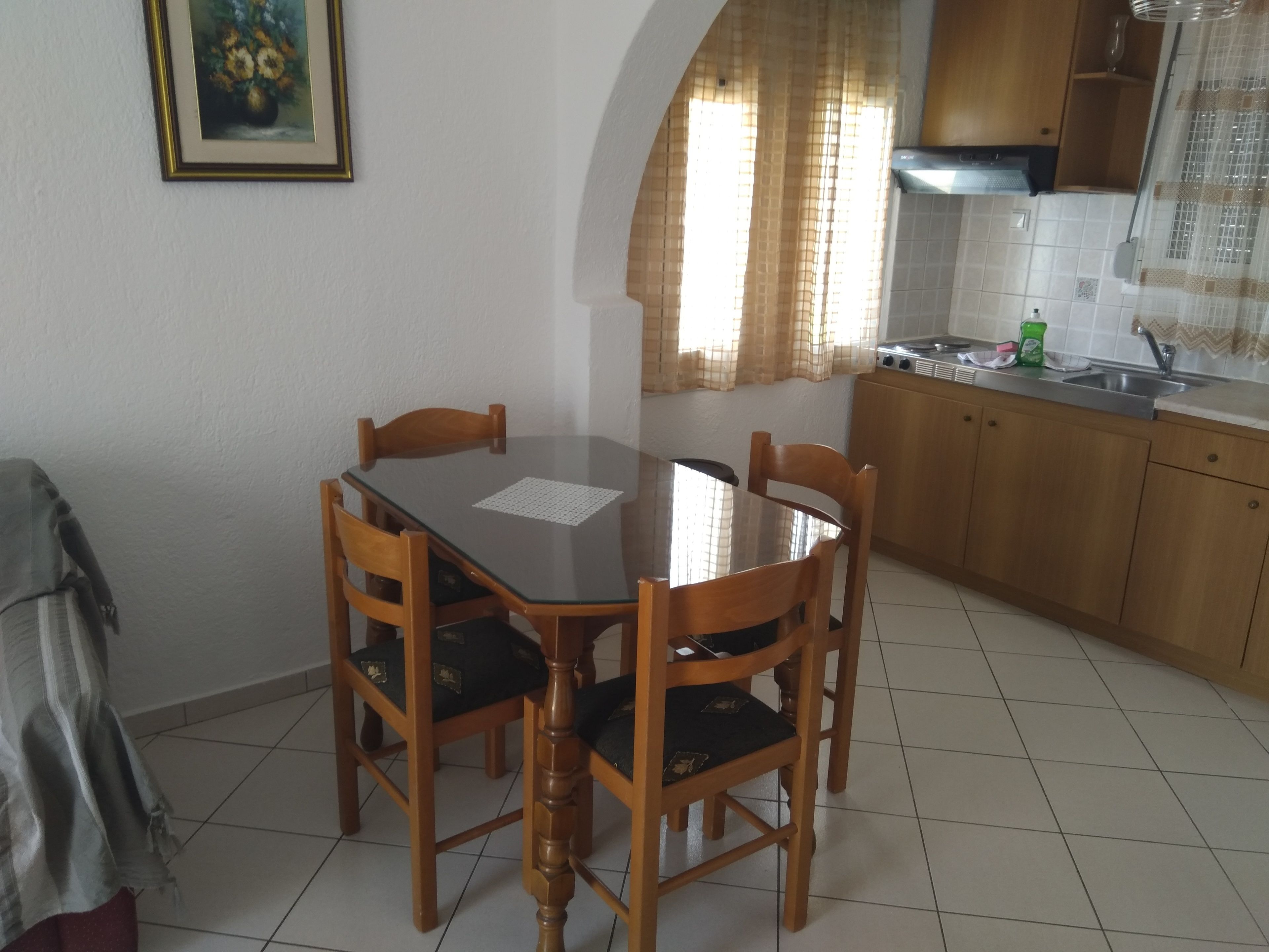 Une table à manger avec quatre chaises, une cuisine avec des meubles en bois et un sol carrelé.