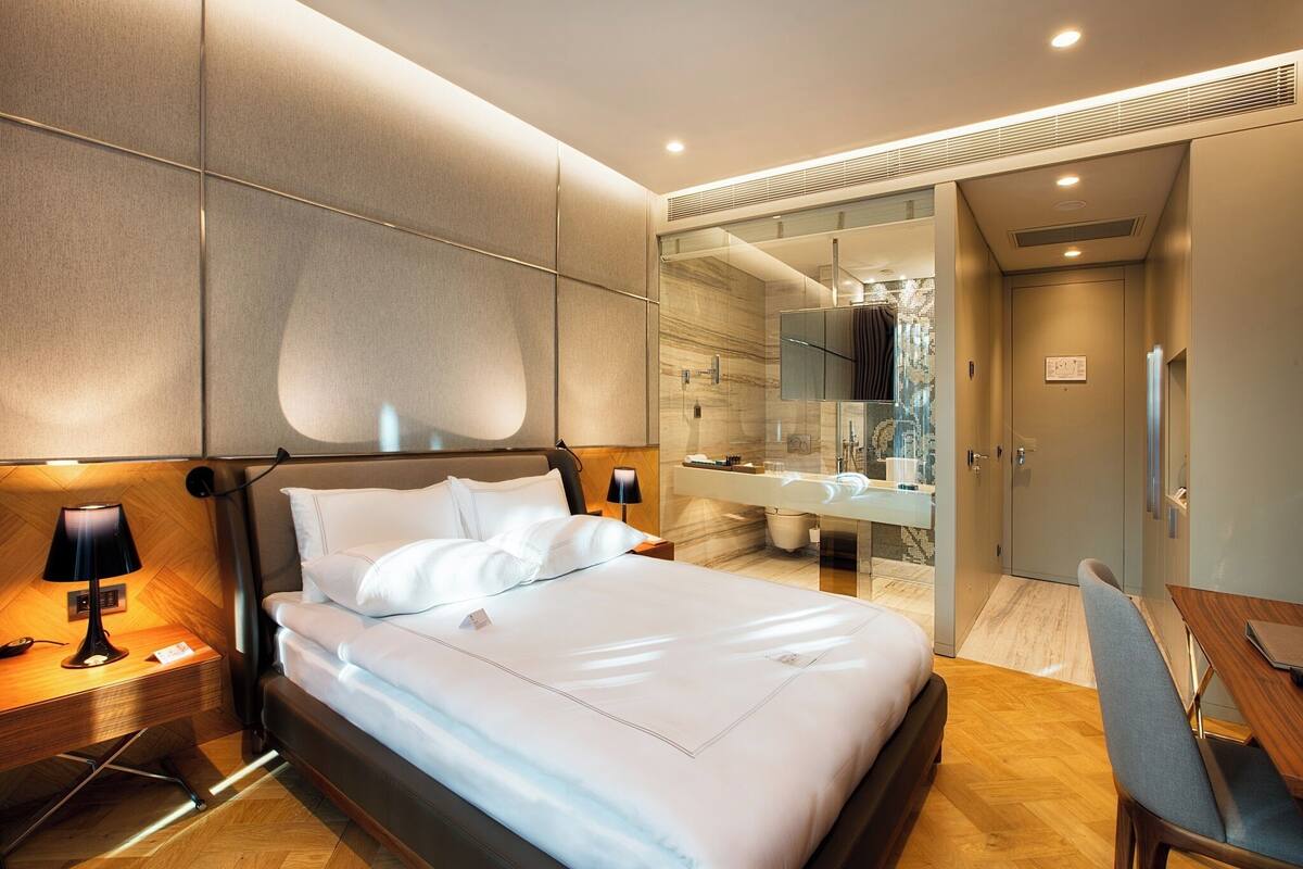 Une chambre d’hôtel moderne dotée d’un grand lit, de tables de chevet, d’un bureau et d’une salle de bain avec un grand miroir et un lavabo.