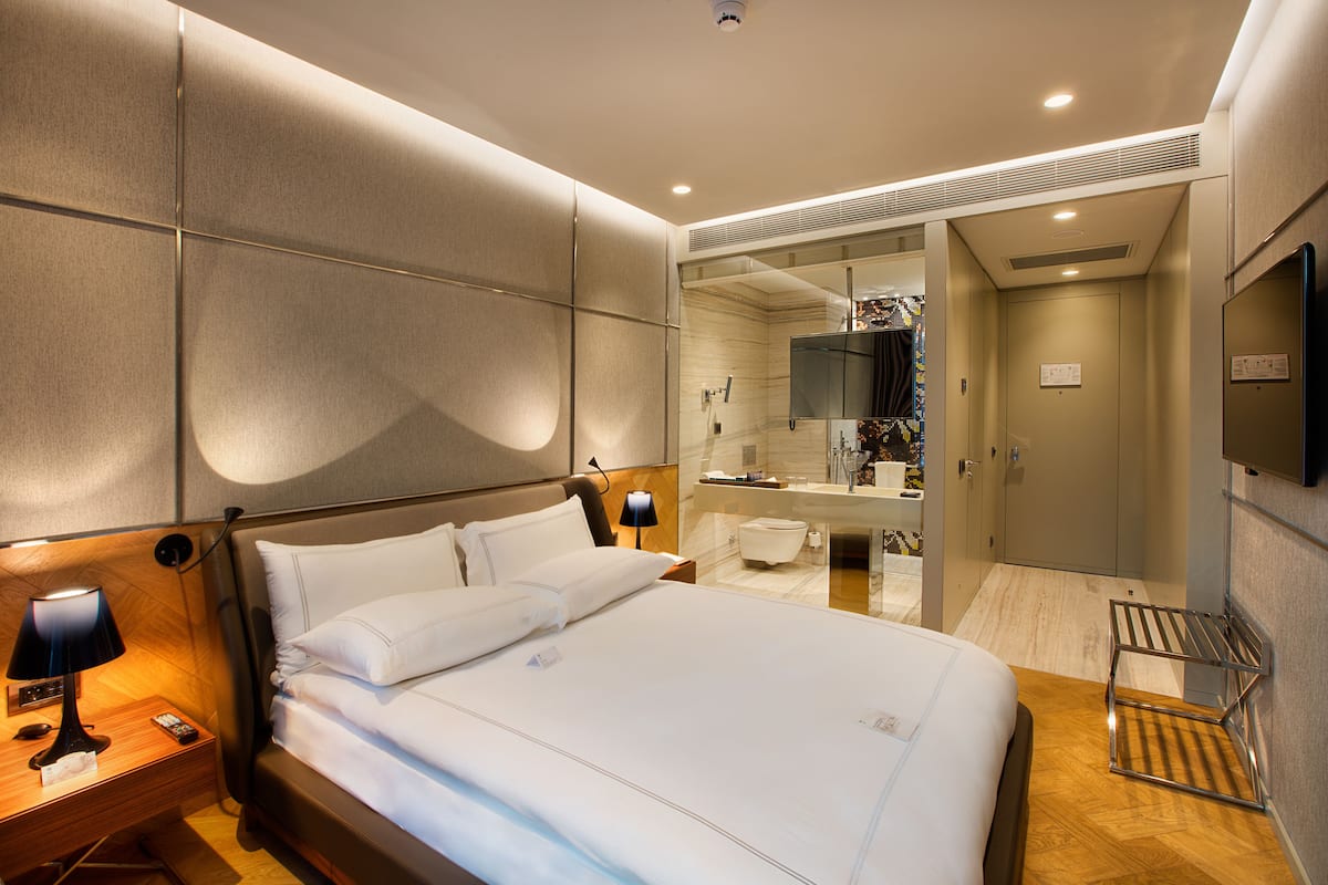Une chambre d’hôtel moderne, dotée d’un grand lit, de tables de chevet, d’un miroir et d’une salle de bain visible à travers une porte ouverte.