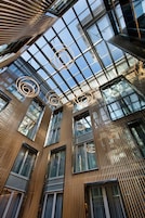 Un edificio moderno con techo de vidrio, listones verticales de madera y luminarias circulares.