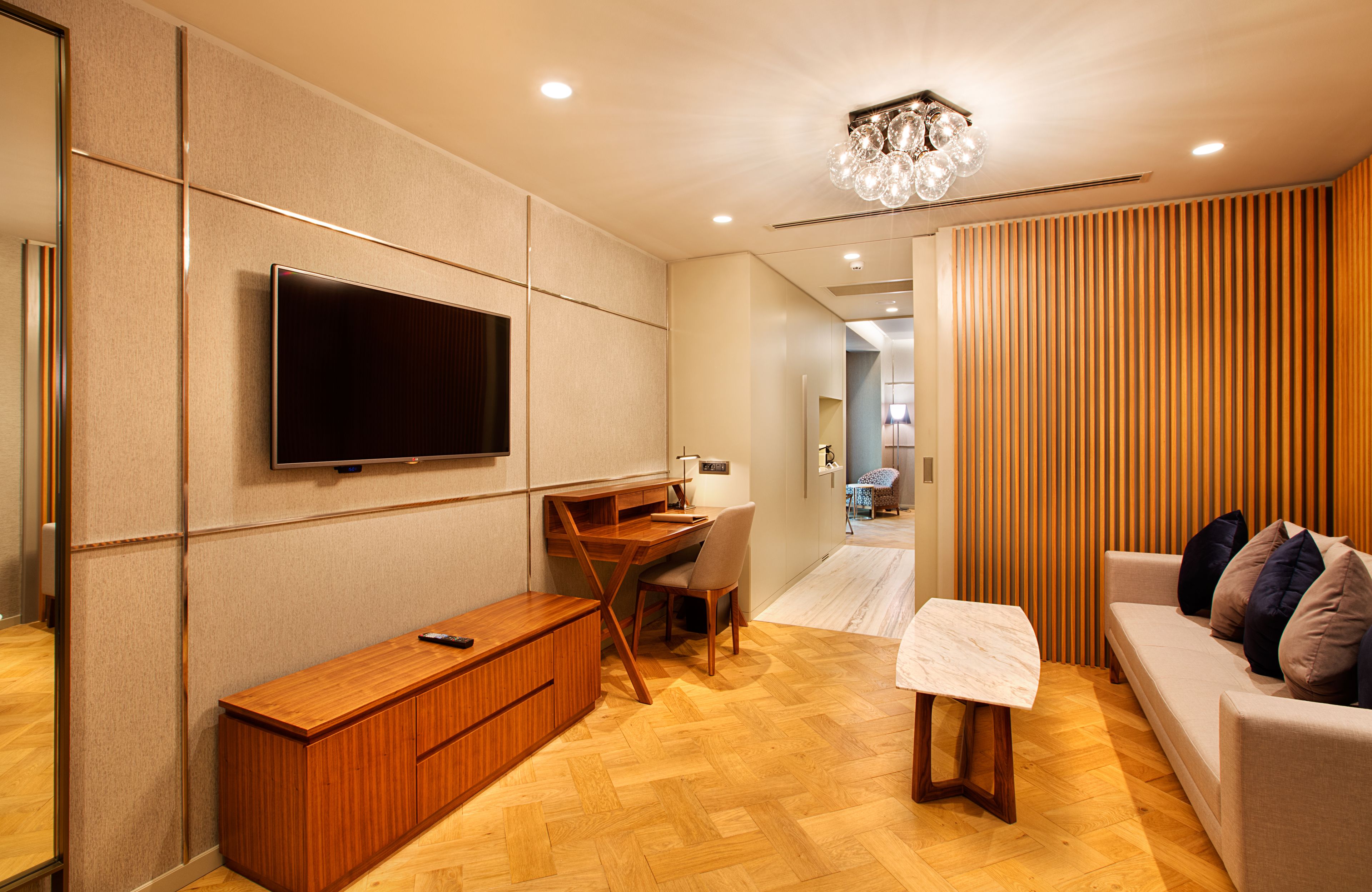 A modern living room with a flat-screen TV mounted on the wall, a wooden desk, a comfortable sofa, and a small table.