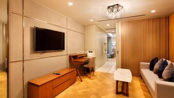 A modern living room with a flat-screen TV mounted on the wall, a wooden desk, a comfortable sofa, and a small table.