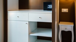 A walk-in closet with a white wardrobe, a small table with a lamp, and a remote control on the shelf. - Guest House Grazioli (Rome)