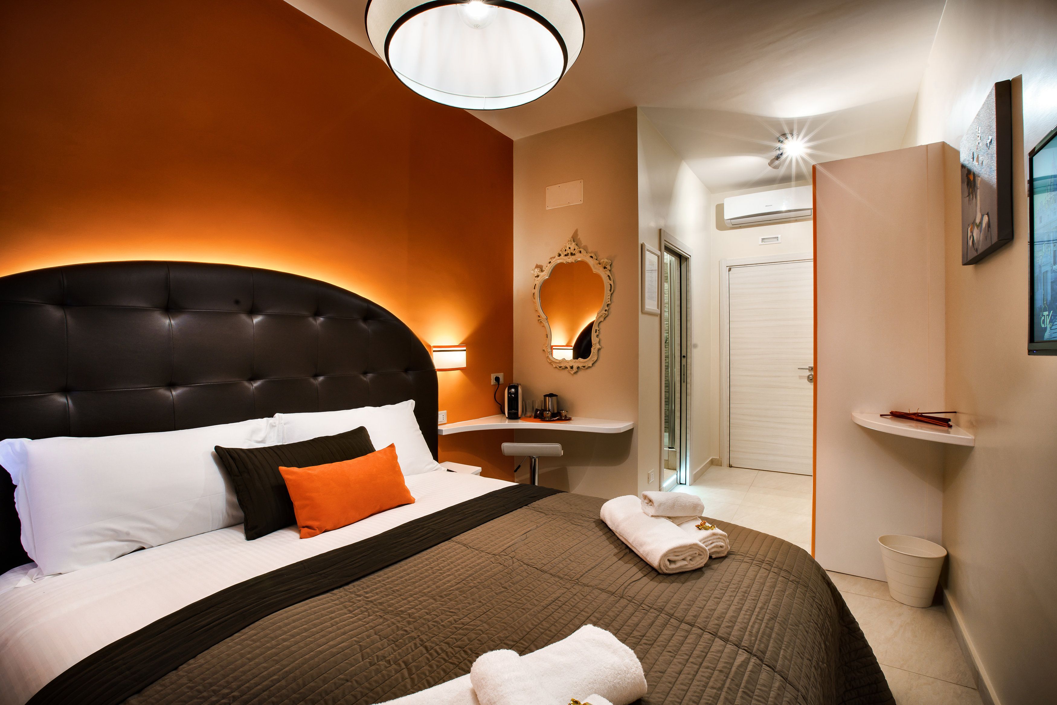 Una habitación de hotel con una cama grande, una mesita de noche, un espejo, una puerta de baño y un perchero para toallas.