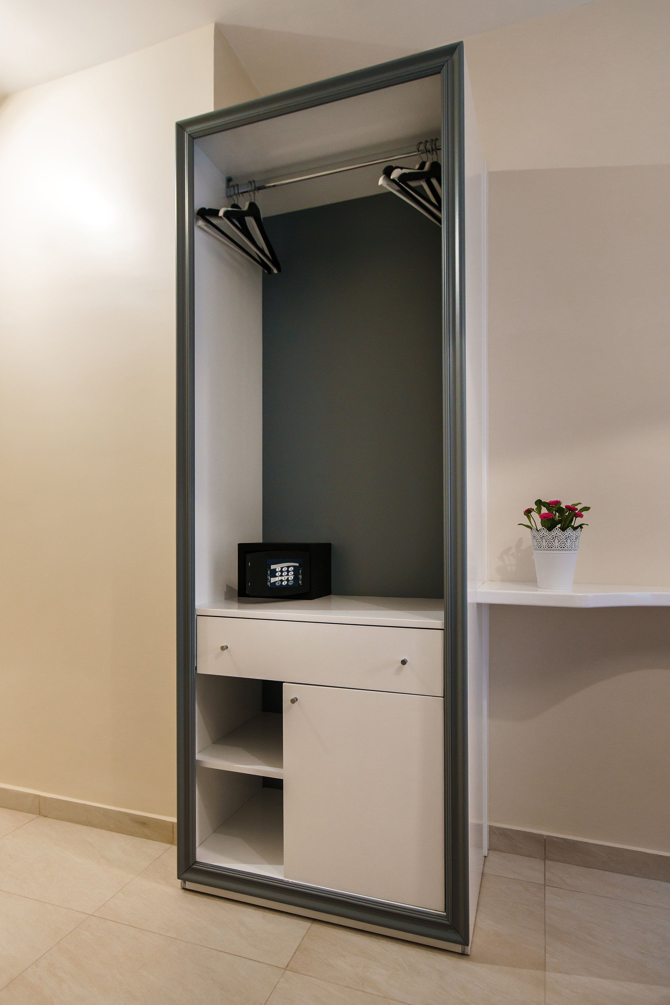 A walk-in closet with a mirror, a hanging rack, and a small shelf with a potted plant.