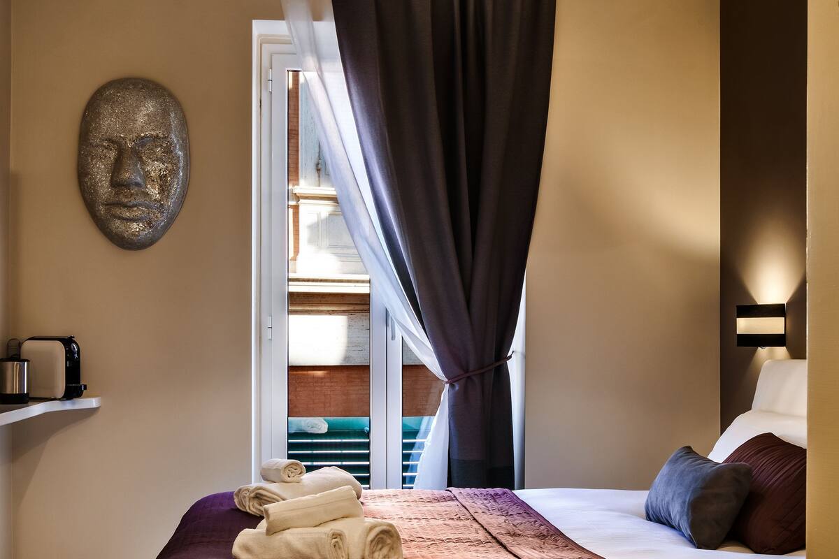 A bedroom with a large bed, a ceiling lamp, a wall-mounted light, and a view of a balcony.