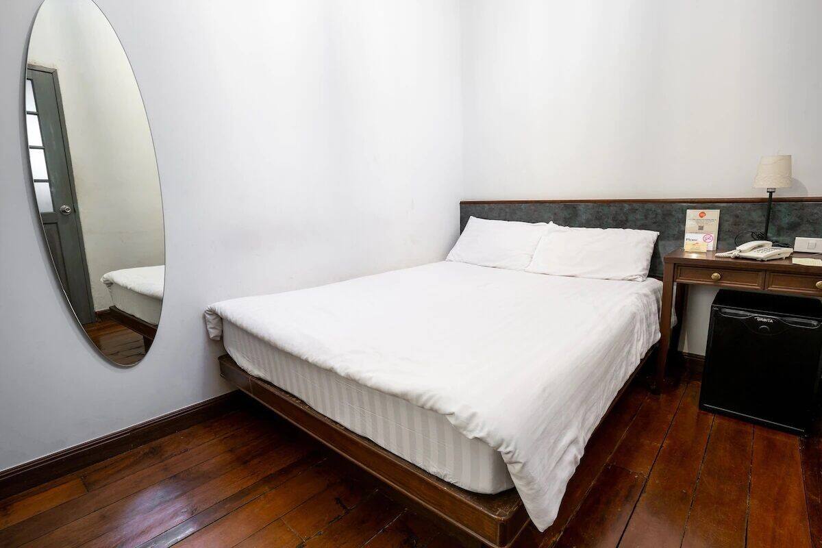 A hotel room with a single bed, a bedside table with a lamp, a telephone, and a small black appliance.