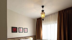 A hotel room with a large bed, a nightstand, a wall-mounted lamp, and a window with curtains. - Chetuphon Gate (Bangkok)