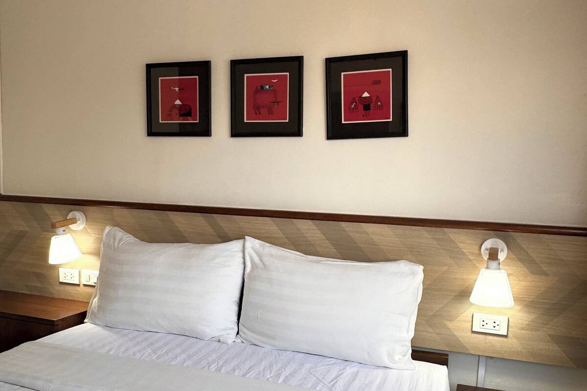 A hotel room with a neatly made bed, three framed artworks on the wall, and bedside lamps.