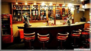 Una zona de bar con mostrador, taburetes y estantes llenos de botellas.