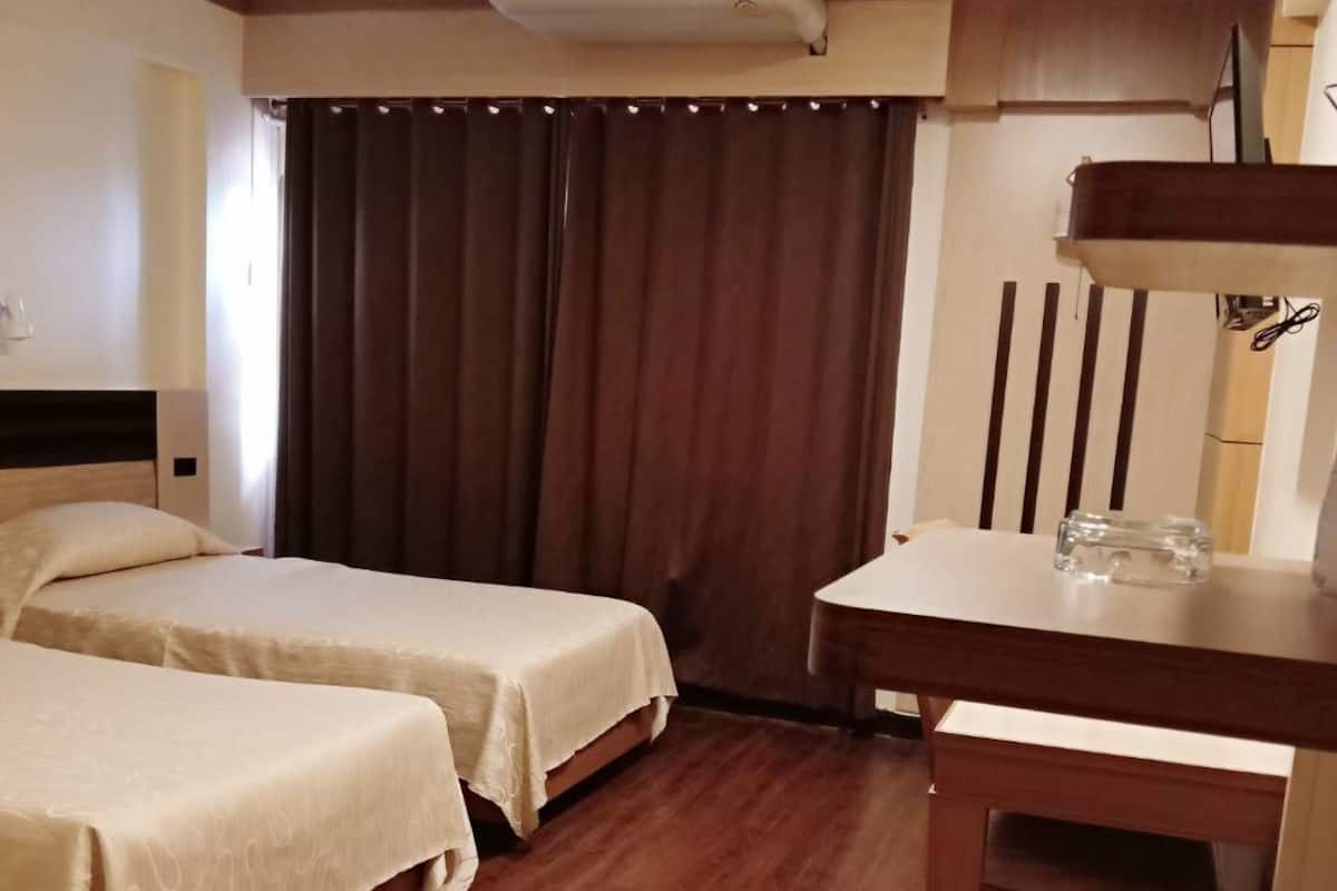 A hotel room with two beds, a desk with a telephone, and an air conditioning unit.
