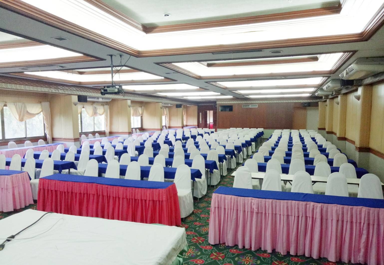 A conference room with rows of tables and chairs, a projector, and a carpeted floor.