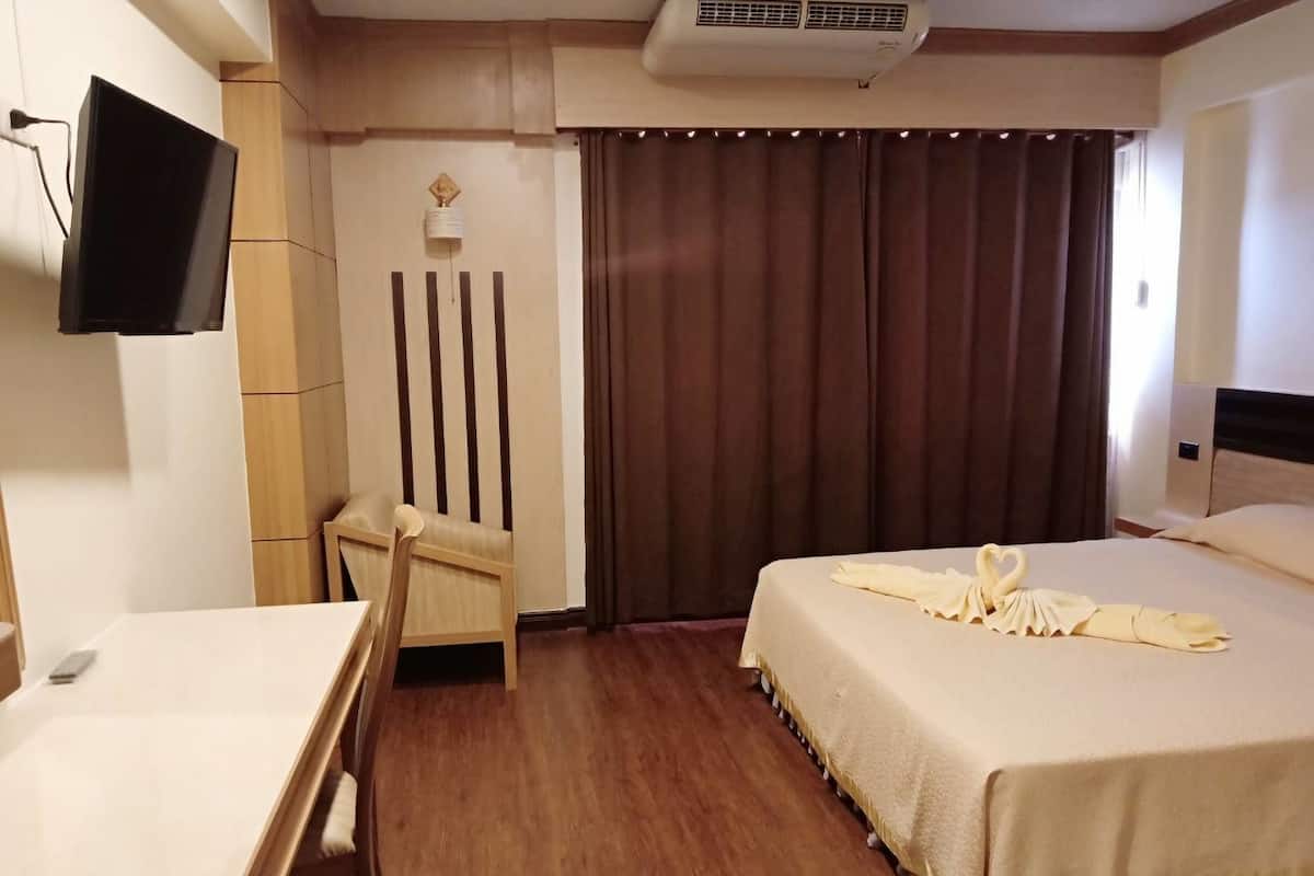 A hotel room with a bed, a desk, a chair, a television, and a curtain.