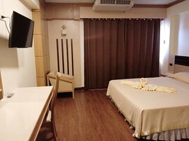 Una habitación de hotel con cama, escritorio, silla, televisor y cortina.