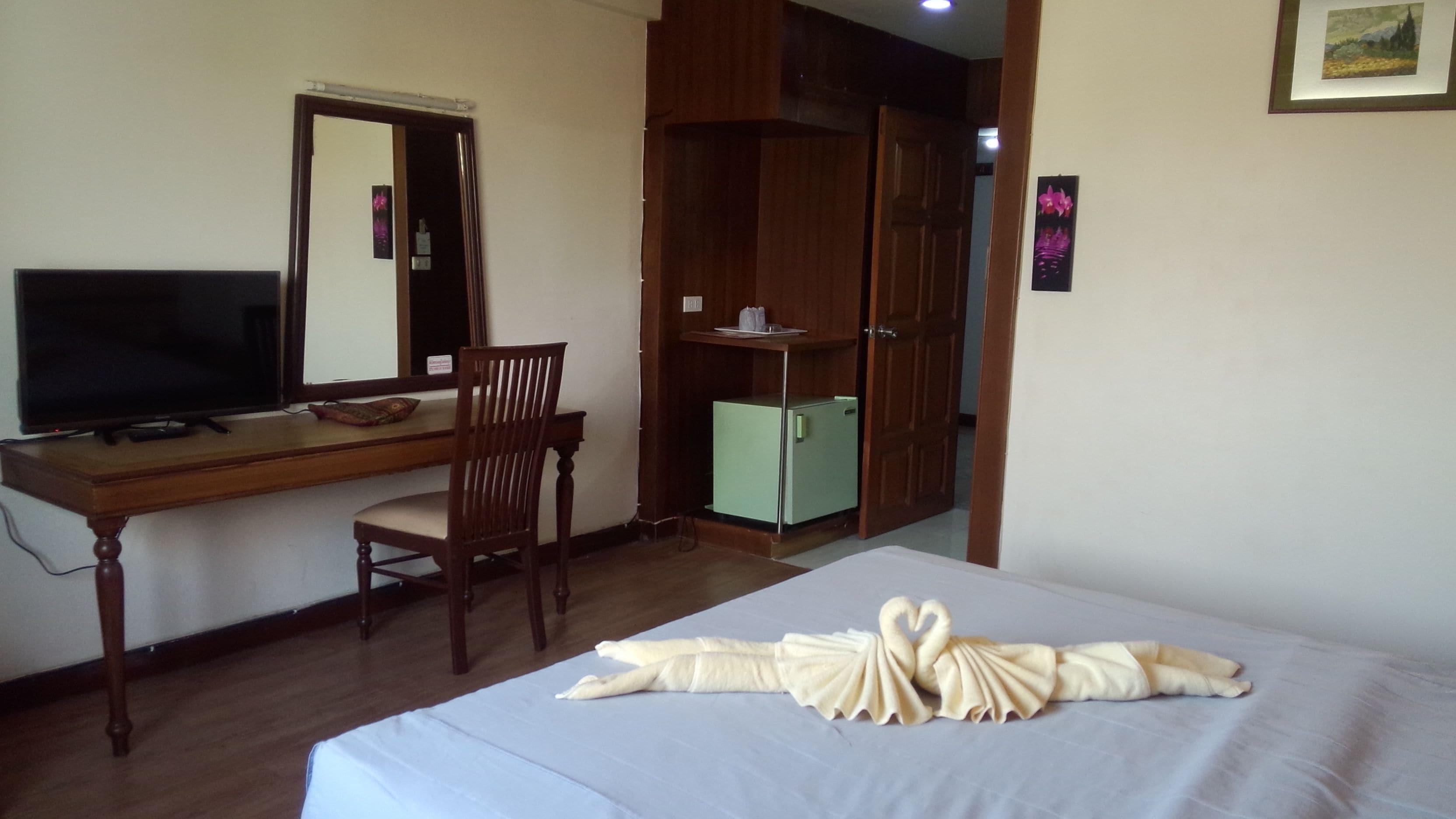 Une chambre d’hôtel comprenant un lit, un bureau avec une télévision, une chaise, une armoire et un petit réfrigérateur.