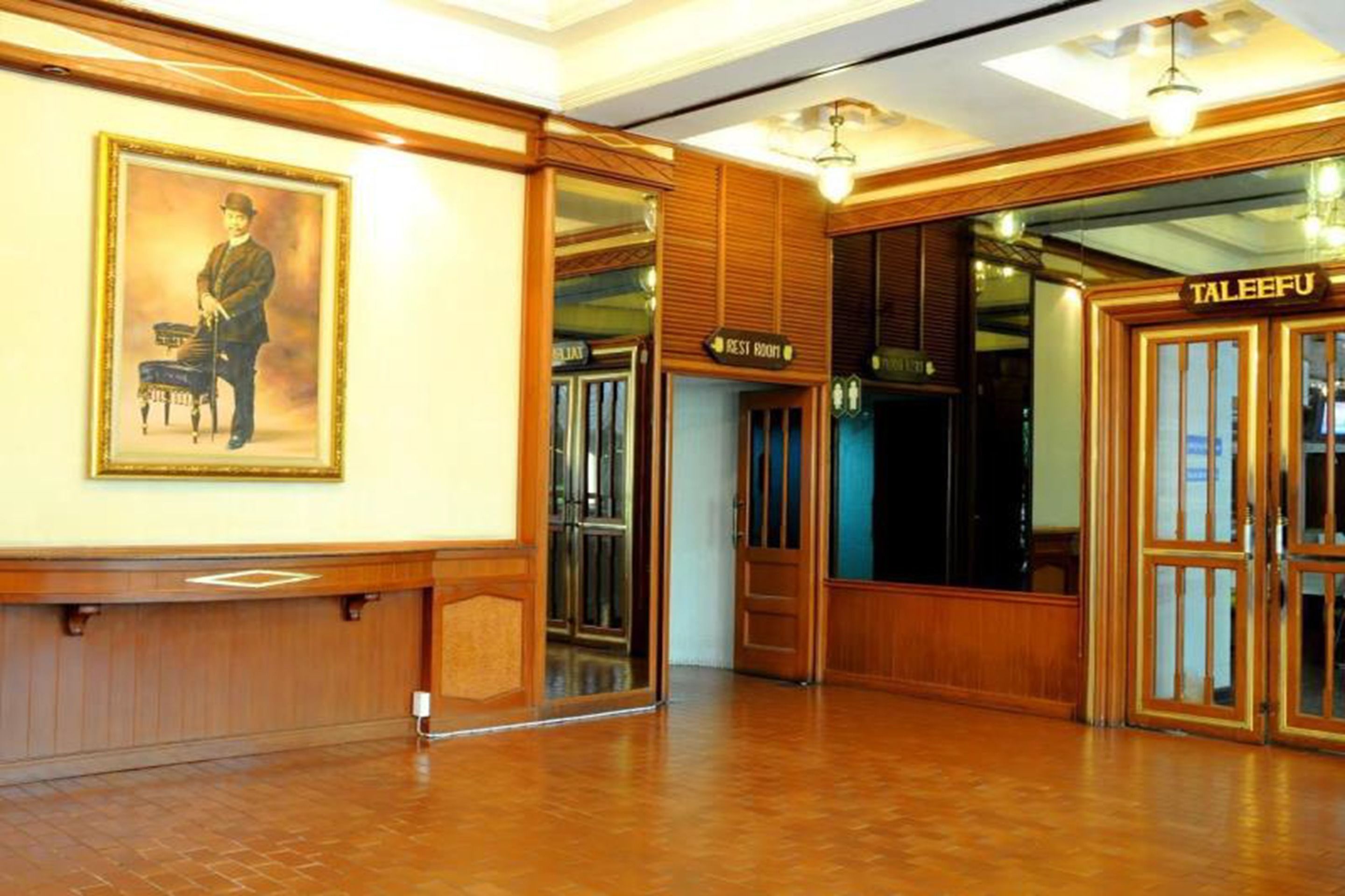 A hotel lobby with wooden paneling, a framed portrait, and a sign for the 'Rest Room'.
