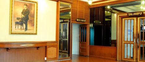 A hotel lobby with wooden paneling, a framed portrait, and a sign for the 'Rest Room'.