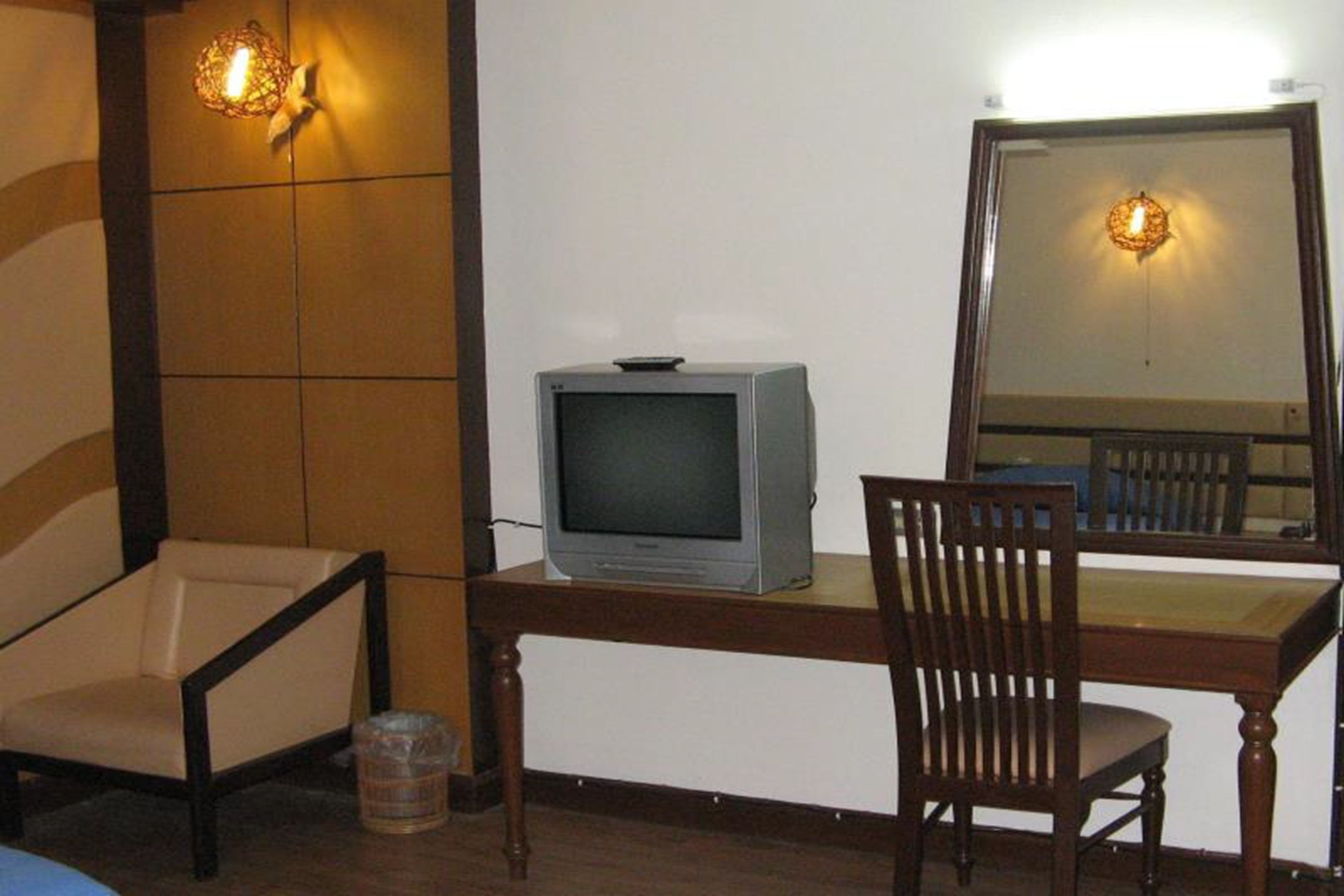 Una habitación con un escritorio de madera, televisor, silla y espejo.