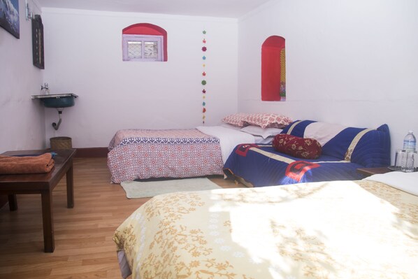 A bedroom with two beds, a wooden table, a sink, and a window with a red frame.