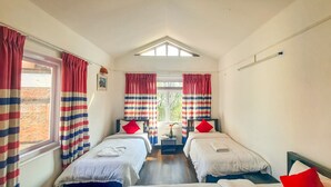 A room with two beds, striped curtains, a skylight, and a view of greenery outside. - Cocina Mitho Chha (Kathmandu)