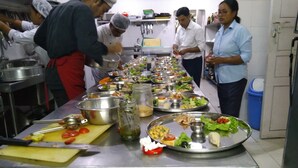 A kitchen with stainless steel countertops, a variety of food items, and kitchen utensils. - Cocina Mitho Chha (Kathmandu)