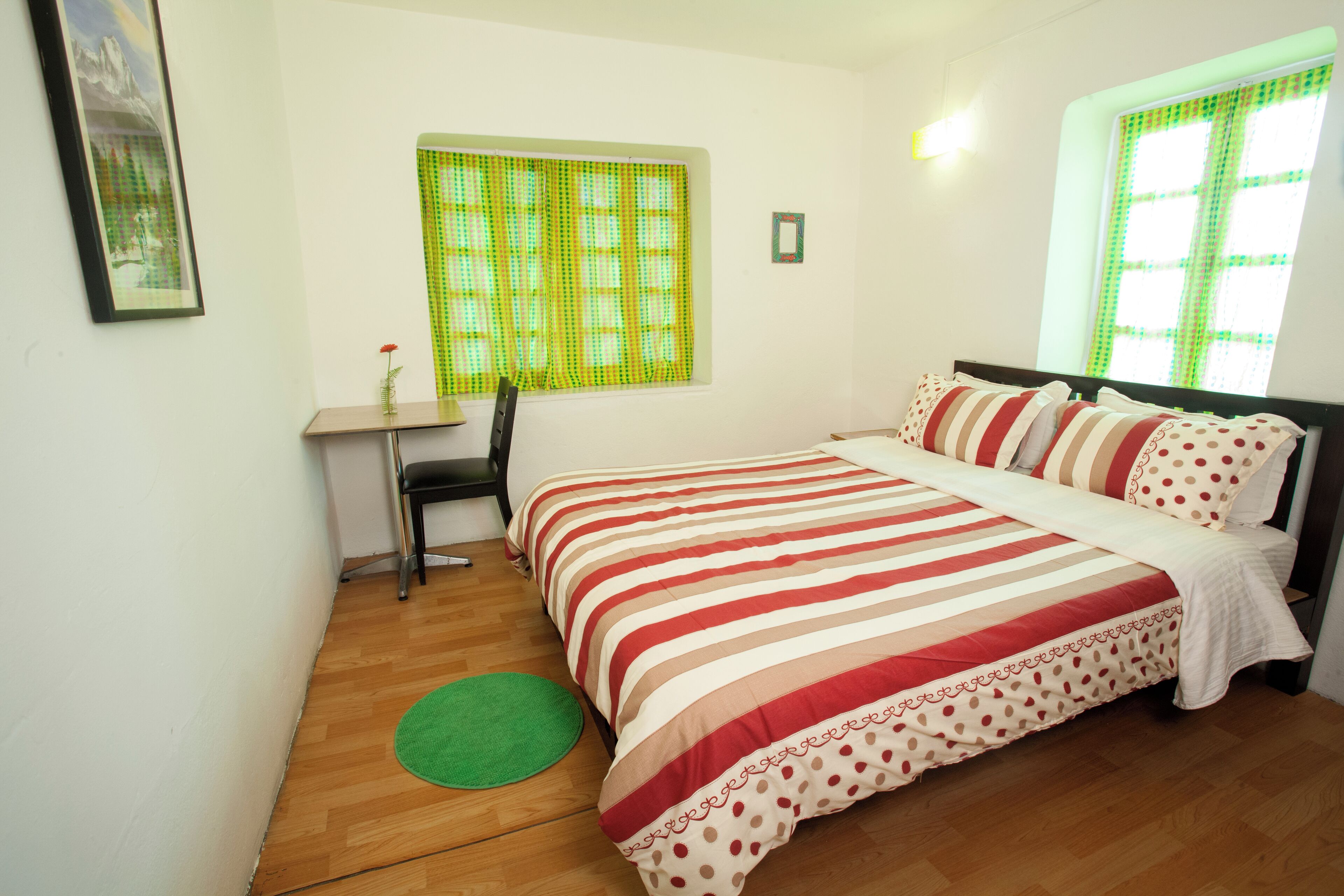 A bedroom with a bed, a desk, a chair, a green rug, and a window with green curtains.