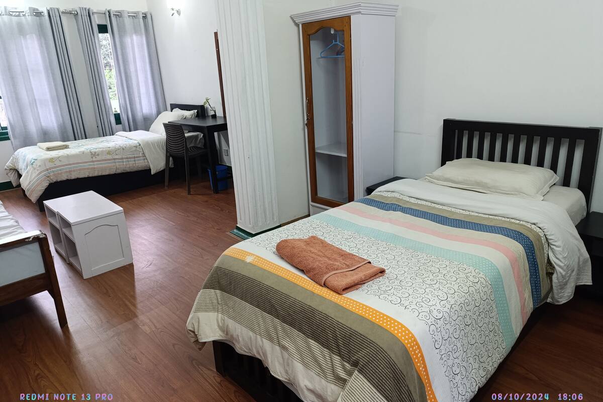 A well-lit bedroom with two beds, a wardrobe, a desk, and a chair.