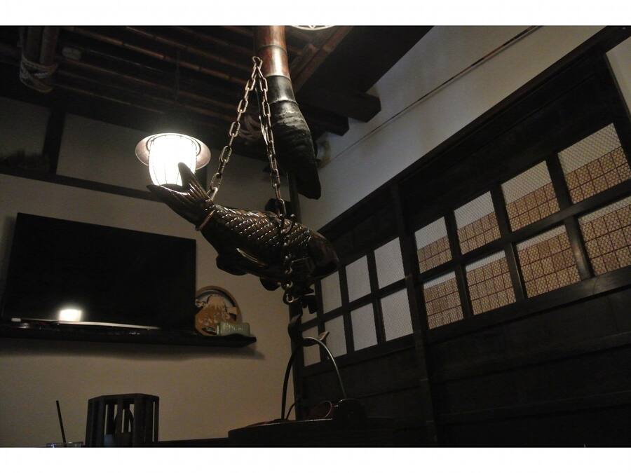 A room with a hanging light fixture, a television mounted on the wall, and a window with a grid pattern.