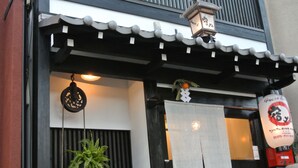 En traditionel japansk bygning med sort-hvid facade, en hængende lygte og et skilt med japanske tegn.