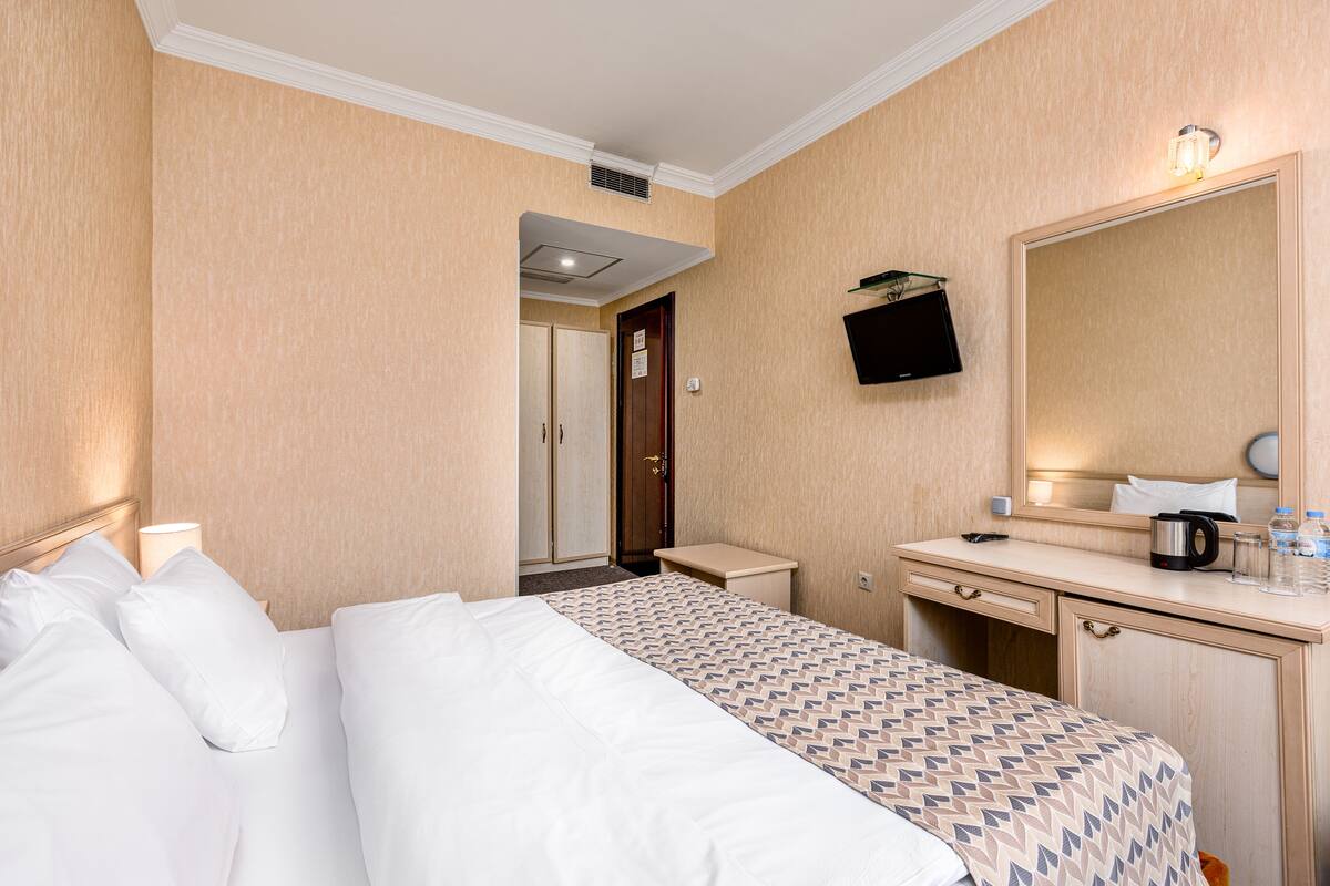 A hotel room with a bed, bedside table, dresser, and a mirror.