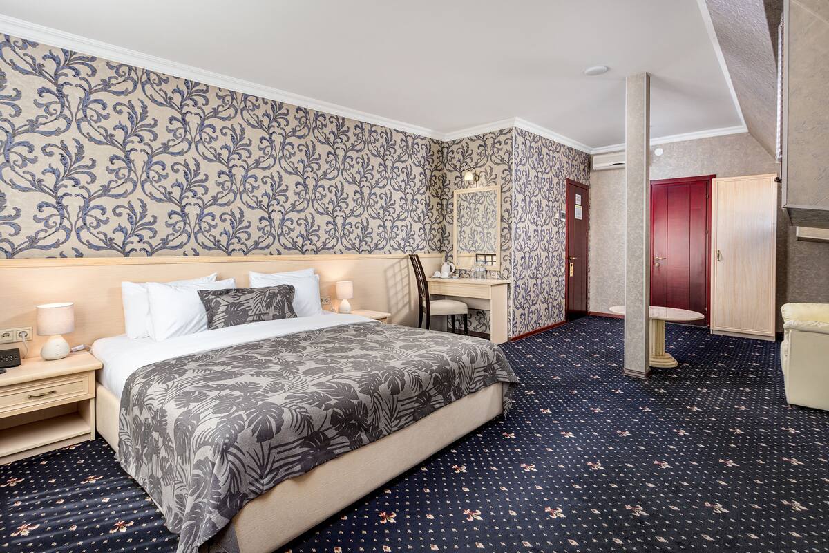 A hotel room with a large bed, a desk, a chair, a mirror, and a wardrobe.
