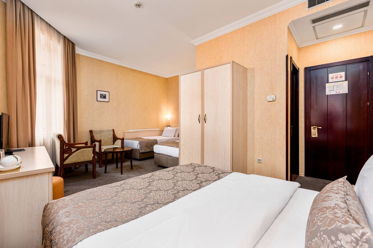 A hotel room with a large bed, a desk, a chair, a wardrobe, and a door with a sign.