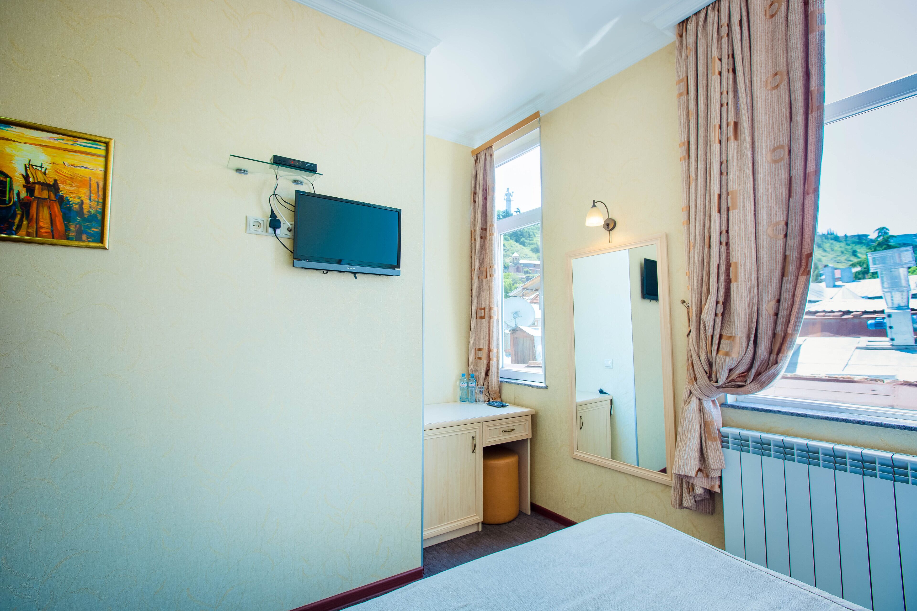 Una camera da letto con un letto, una televisione a parete, una finestra con tende e un termosifone.