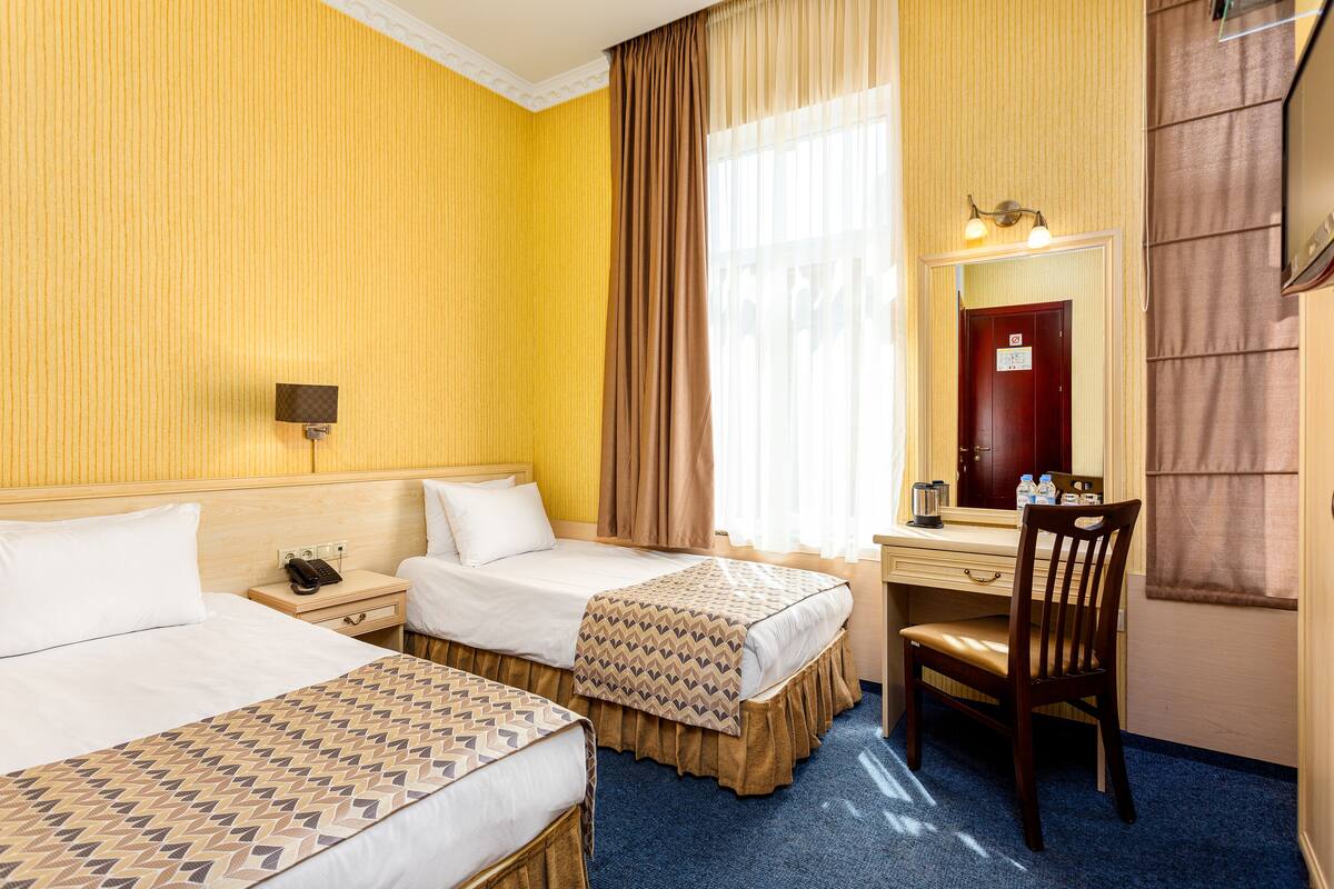 A hotel room with two beds, a desk, a chair, a mirror, and a window with curtains.