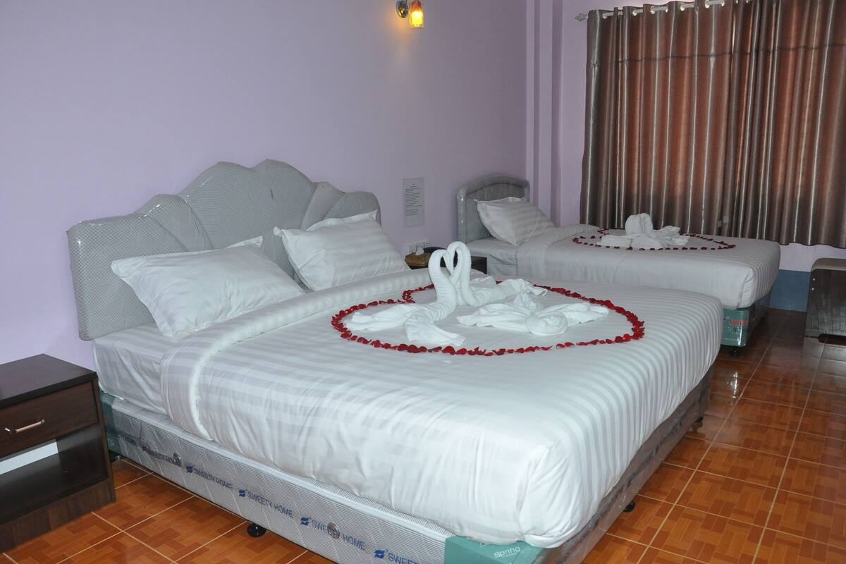 A hotel room with two beds, each adorned with white linens and red flower garlands.