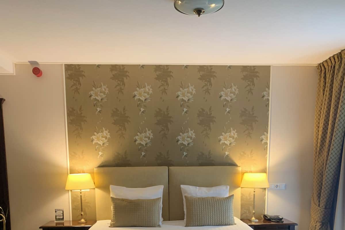 Ein Hotelzimmer mit einem großen Bett, zwei Nachttischlampen, einem blumengemusterten Kopfteil und einem grünen Teppich.