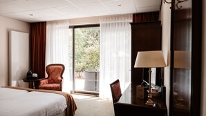 A hotel room with a bed, a chair, a desk with a lamp, and a view of greenery outside. - De Lunterse Boer (Lunteren)