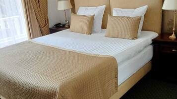 A neatly made bed with a beige bedspread and pillows, a wooden headboard, and a green carpeted floor.