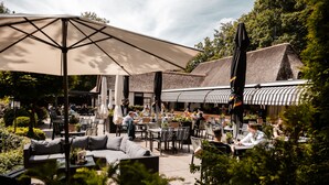 An outdoor patio area with seating arrangements, including sofas and tables, under large umbrellas. - De Lunterse Boer (Lunteren)