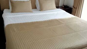 A neatly made bed with a quilted brown bedspread and white pillows, a floral wallpaper headboard, and a bedside lamp.